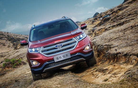 A red Ford Edge with Chinese license plates, on rocky terrain.