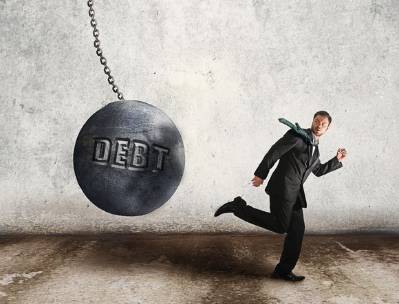 Businessman running from giant ball on chain with debt engraved on it