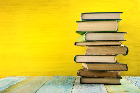 Old hardcover books haphazardly stacked in front of yellow background.