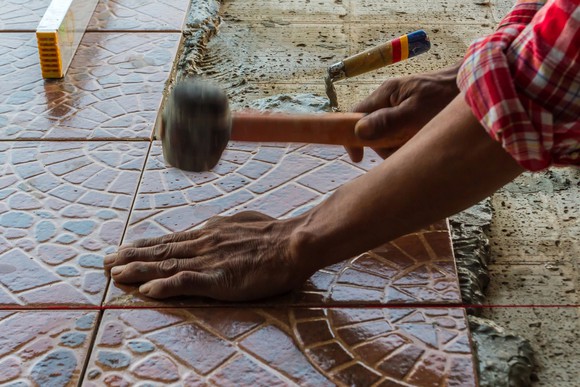 A person using a rubber mallet to install floor tile.