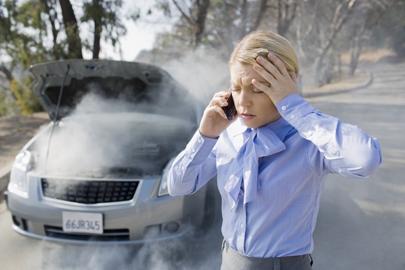 Frustrated-looking woman in front of overheating car.