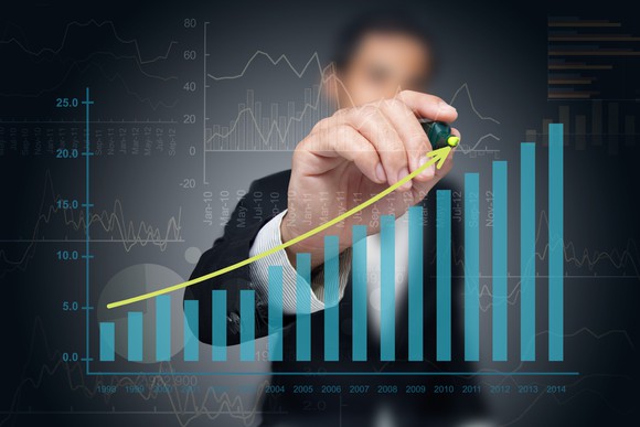 A businessman drawing a line upward above a chart of ascending columns.