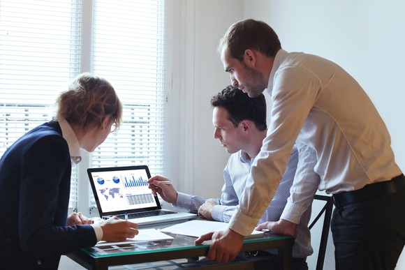 Three people look at information on a laptop screen.