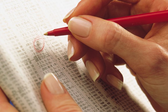 A person circling stocks in a financial newspaper.