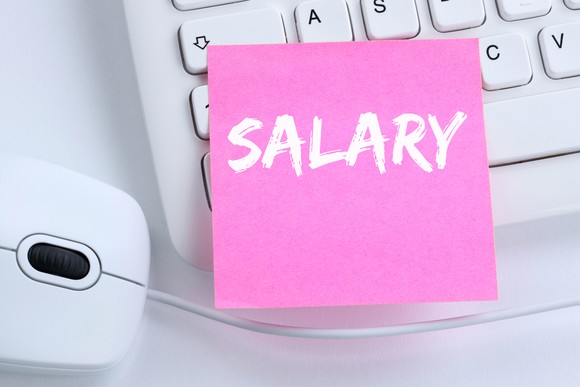 Pink post-it with the word "salary" stuck on a keyboard next to a mouse