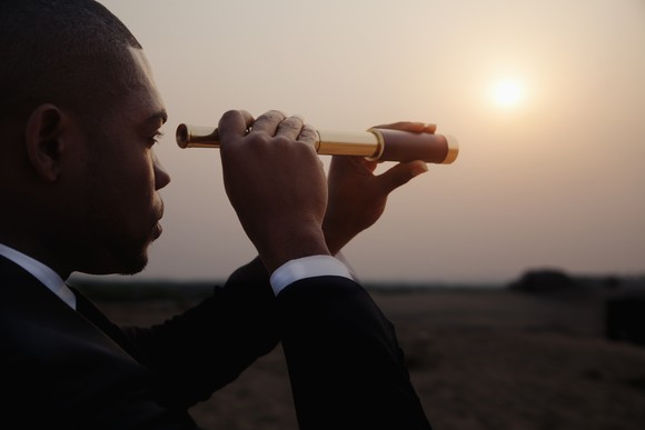 Man in business suit looking through telescope toward sunset