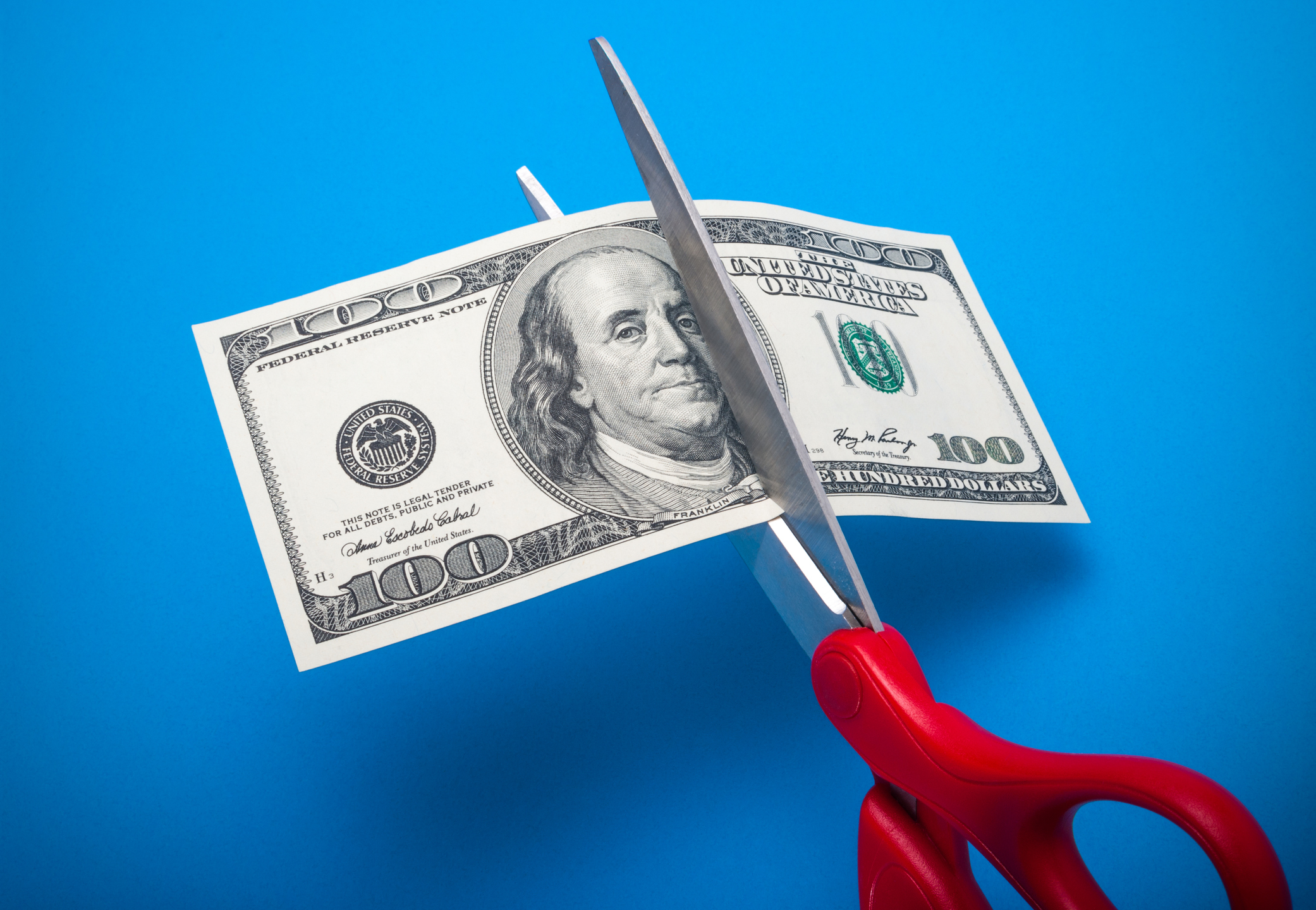 A pair of scissors cutting a $100 bill.
