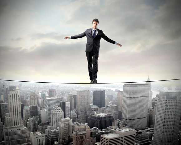 A businessman balances on a high wire between two skyscrapers.