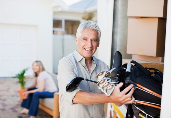 An older man smiling as he grabs his golf clubs.