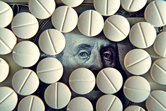 Prescription pills covering a hundred dollar bill, with only Ben Franklin's eyes exposed.