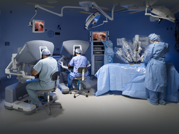 Several surgeons and a robotic surgical system in an operating room.