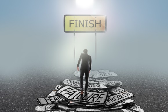 A businessman walks over signs displaying words of failure towards a finish line.