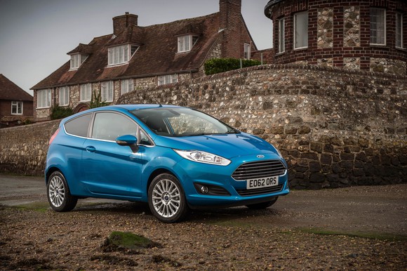 A teal Ford Fiesta two-door hatchback in front of a stone building in Europe.