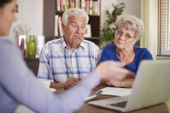 Senior man looking shocked and senior woman looking concerned as material is presented on a laptop by a third party