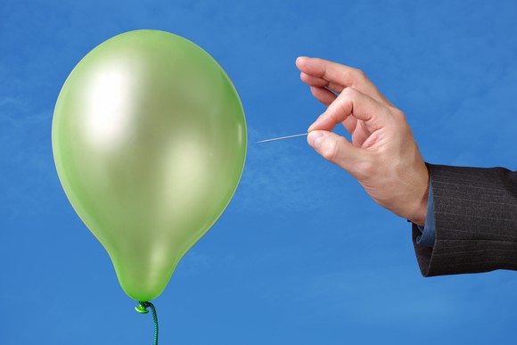 a hand popping a green balloon with a pin