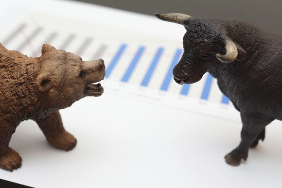 Bear and bull figurines facing each other on top of a sheet of paper containing a chart.