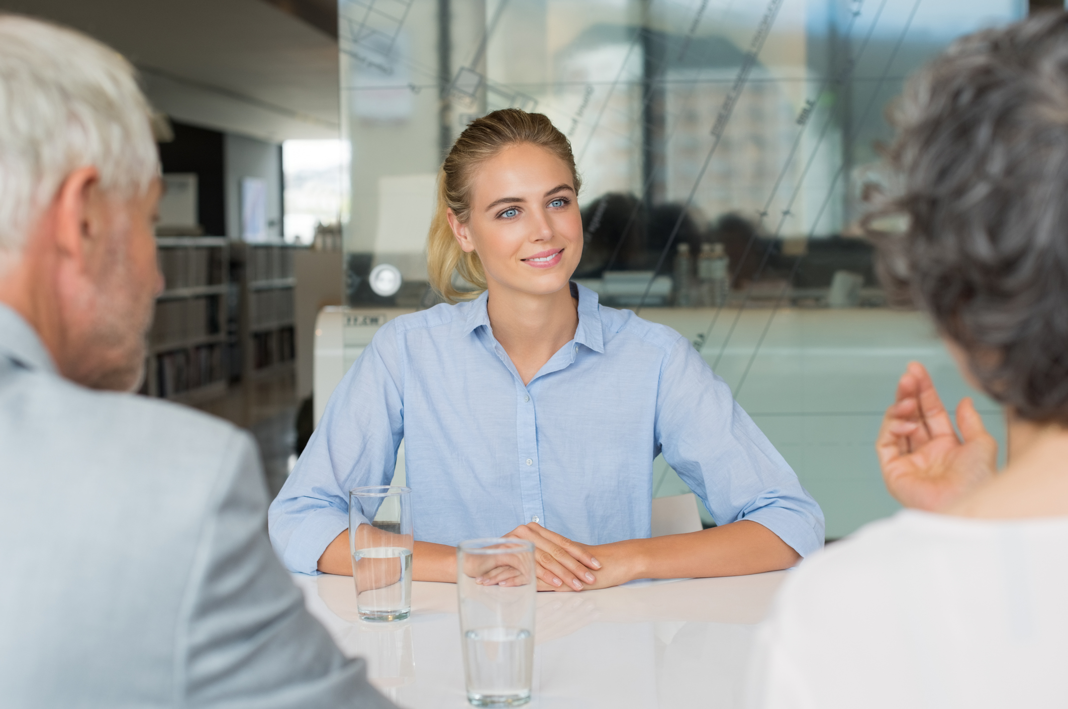 Smiling woman in collared shirt facing two individuals.