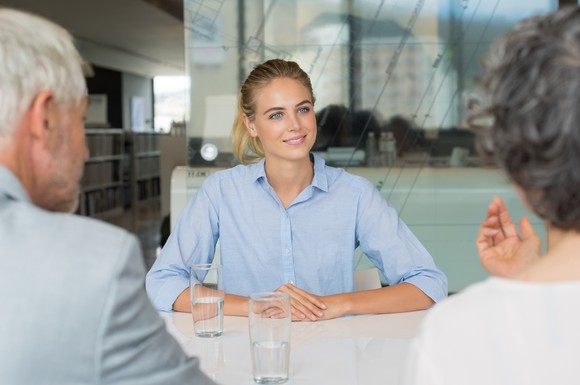 Smiling woman in collared shirt facing two individuals.