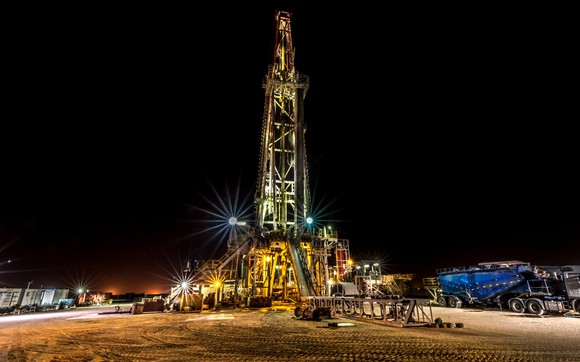An illuminated drilling rig at night.