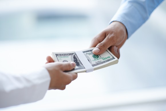 Two men exchanging a stack of $100 bills between them