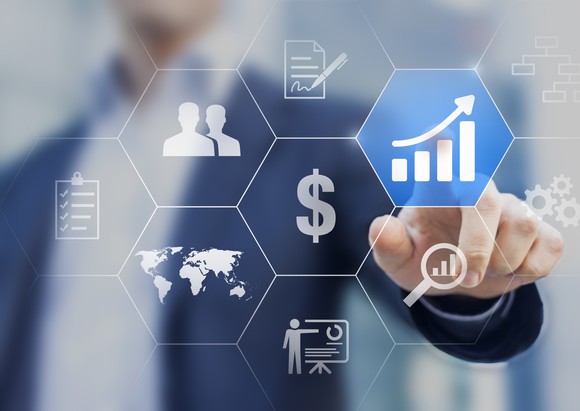 On a transparent touchscreen with a cluster of hexagonal icons, a man points to an icon showing a rising bar chart.