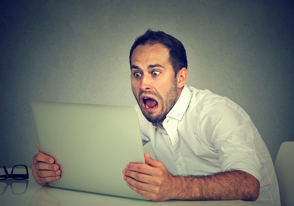 A man clutches a tablet and looks at it with an open-mouthed, terrified expression.