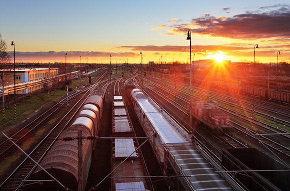 Freight trains at a station with the sun setting in the background.