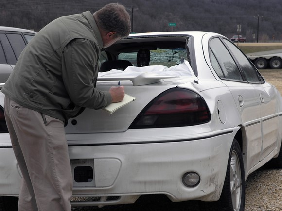 Man writing on a notepad on a car that's just been in an auto accident.