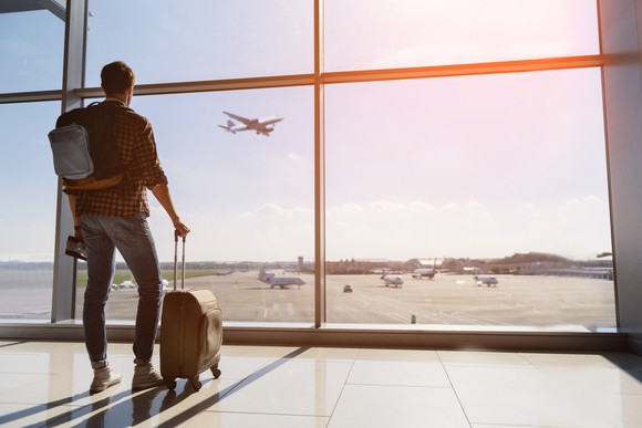 A young man stands in an airport and watches a plane takeoff.