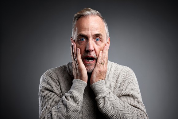 Surprised grey-haired man with hands on his cheeks