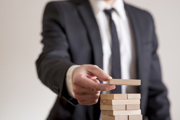 A man in a business suit building a tower of wooden blocks