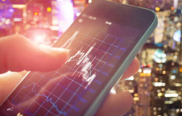 Close up of a finger placing a stock trade by clicking on a chart displayed on smart phone.