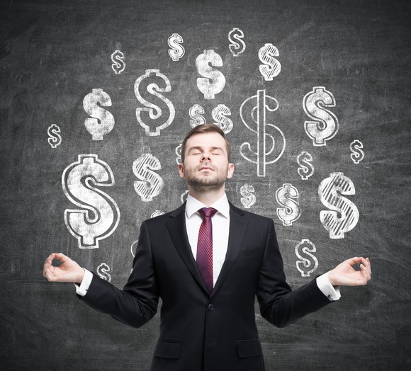 Man meditating in front of dollar signs