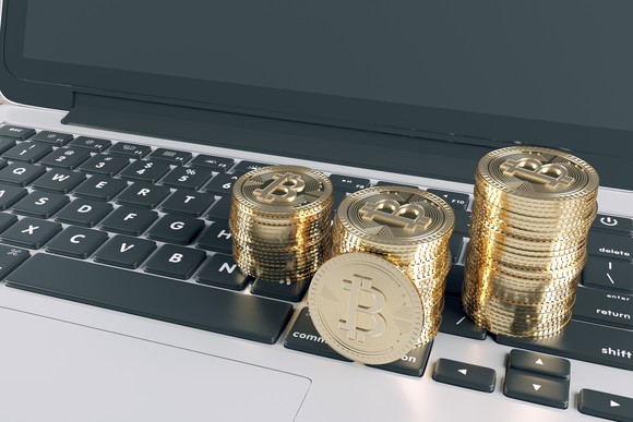 Gold coins representing bitcoins, stacked on a computer keyboard.