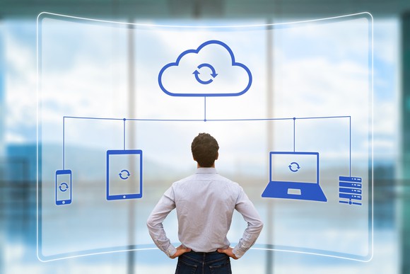 A man looking at a visualization of several electronic devices syncing in the cloud.