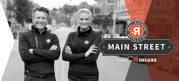 Robert Hervajec and Amanda Brinkman in matching outfits on a Main Street in a small town, with graphics for Deluxe's Small Business Revolution program.