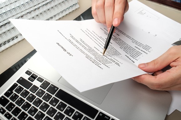 Hand with pen editing a printed resume on top of a laptop.