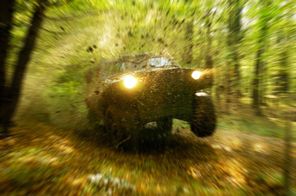 Military all-terrain vehicle speeding through the woods splattering earth.