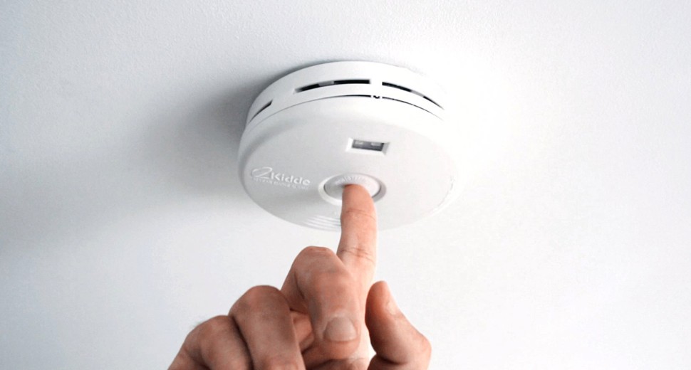 A person pushing the test button on a smoke alarm.