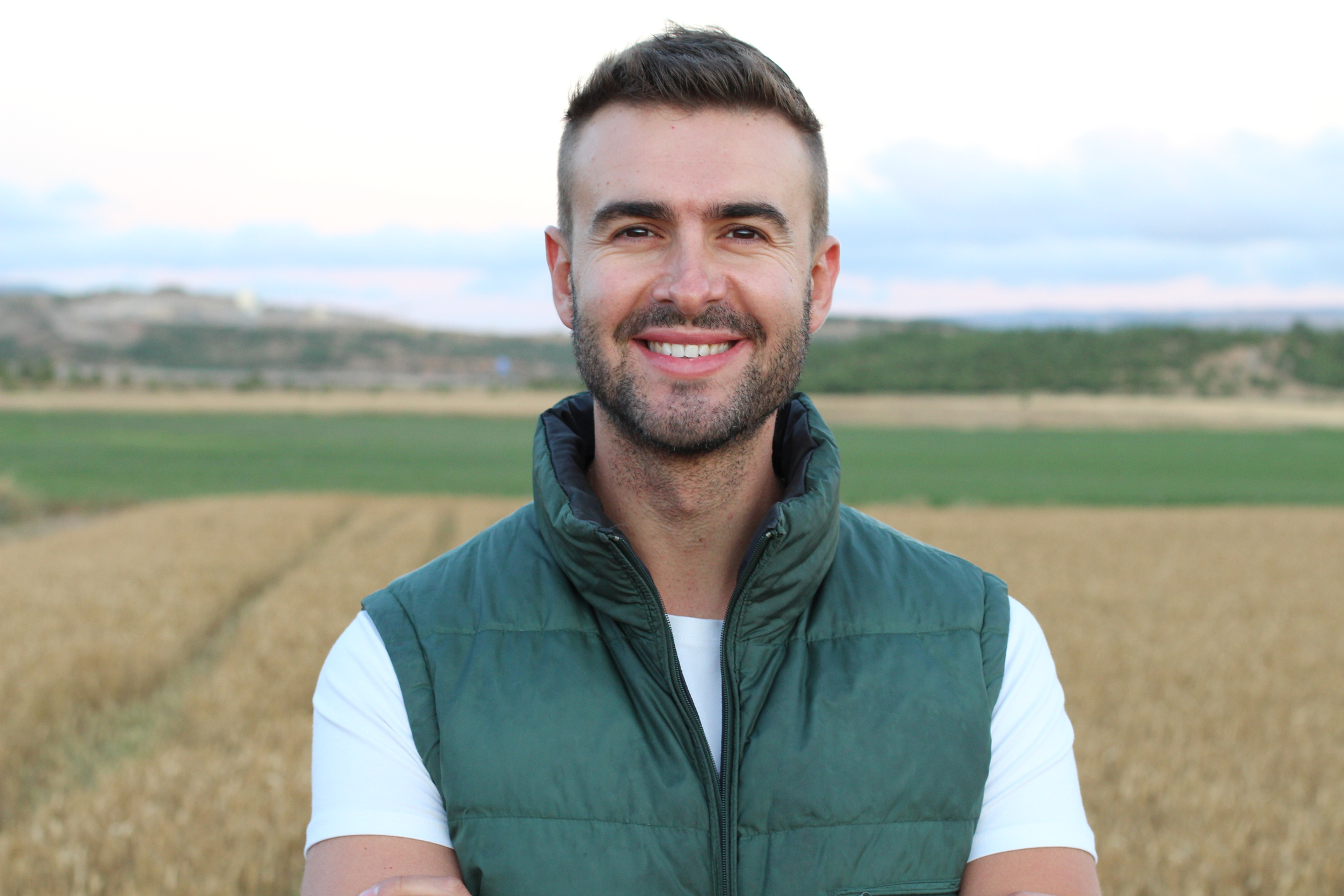 A smiling man outdoors wearing a green vest