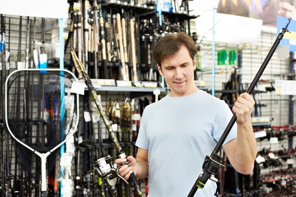 A man holds up two fishing rods inside of a store.