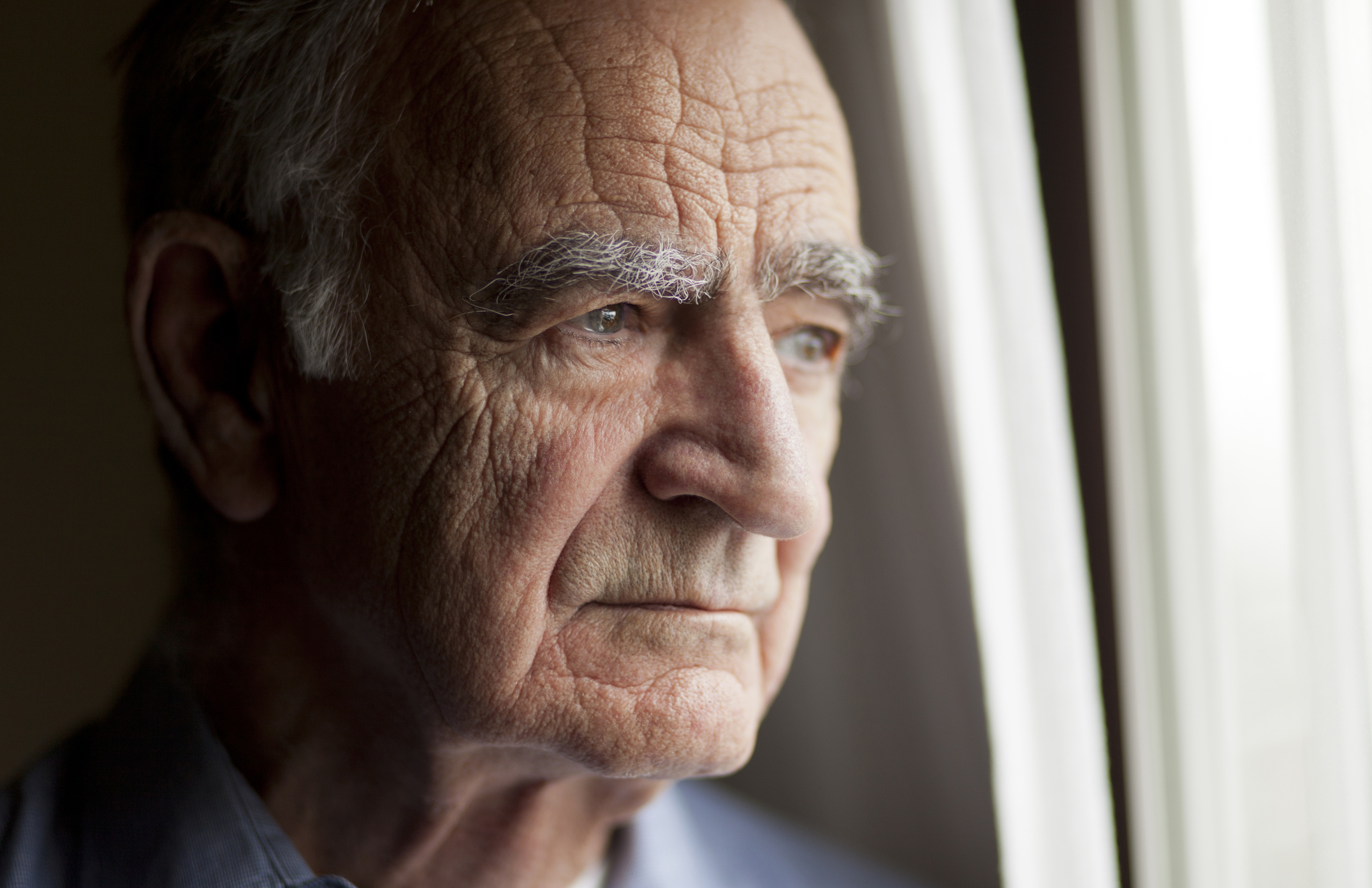 An elderly man in deep thought while staring out his window.