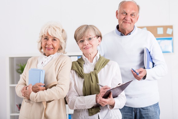 Three senior citizens holding notebooks and pens as if ready to take notes.