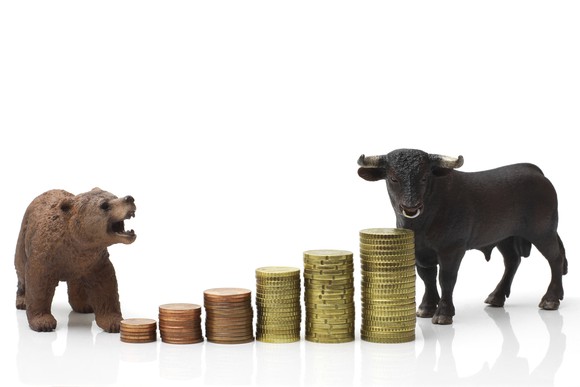 Bear and bull standing near a growing stack of coins