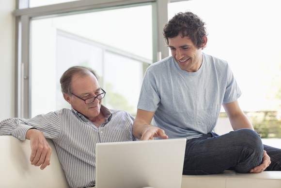 A father and son chatting in front of a laptop.