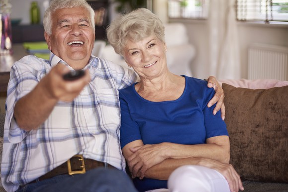 Senior male with TV remove laughing and putting his arm around a senior woman