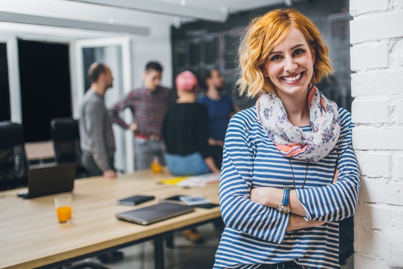 Smiling woman leaning against a brick wall with a group of people in the background