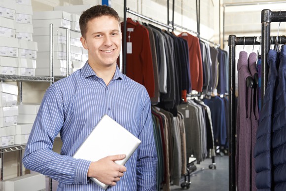 A warehouse worker stands among clothes.
