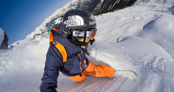 A snowboarder with a mounted GoPro as he goes down a ski slope.