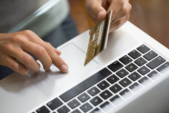 A hand holds a credit card over a laptop.